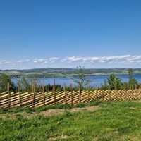 Skigard med brun impregnert skigardstaur, bundet sammen med ståltråd som har utsikt over Mjøsa